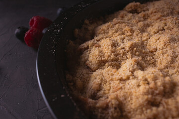 Homemade apple crumble with berries in low light. Dark food photo with copy space.