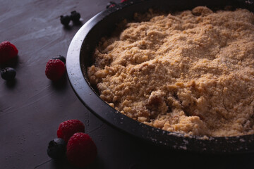 Homemade apple crumble with berries in low light. Dark food photo with copy space.