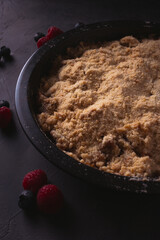 Homemade apple crumble with berries in low light. Dark food photo with copy space.