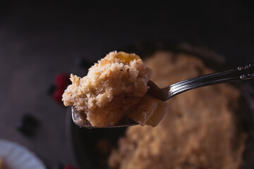 Spoon showing a piece of homemade apple crumble in low light. Dark food photo with copy space.