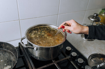 The girl, the cook, prepares soup from vegetables in boiling water, stirring the water in a...