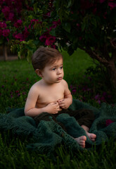 baby boy is sitting in garden under the bush and  looking surprised somewhere 