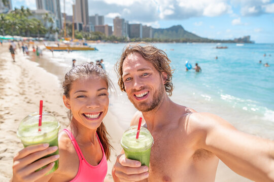 Healthy food happy fit young couple drinking green smoothie juice breakfast running on Waikiki Beach, Honolulu, Hawaii travel vacation. Summer lifestyle active people