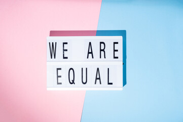 We are equal text on the lightbox. Concept of feminism on a blue and pink background. Top view
