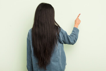 hispanic pretty woman standing and pointing to object on copy space, rear view