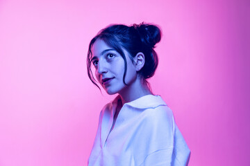 Half-length portrait of young beautiful girl in white blouse posing isolated on pink background in neon light. Concept of emotions