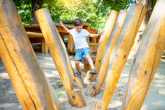 Children's obstacle course on a modern playground. Kid crossing a wooden bridge using his body balance. Development of the child's agility and courage.