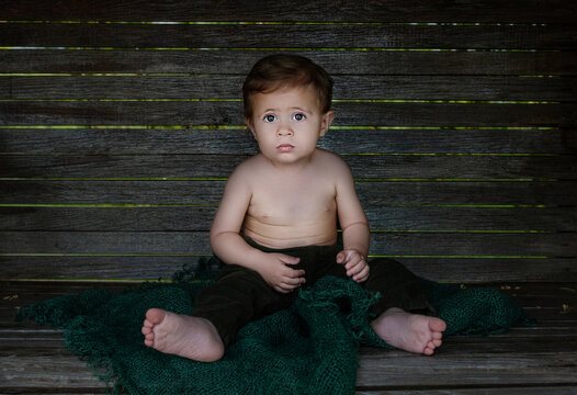 Bbaby boy is naked, he is  sitting on wooden swing 