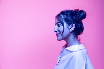 Half-length portrait of young beautiful girl in white blouse posing isolated on pink background in neon light. Concept of emotions