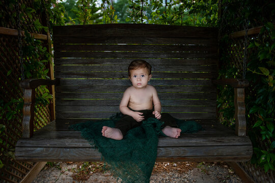  Bbaby boy is naked, he is sitting on wooden swing