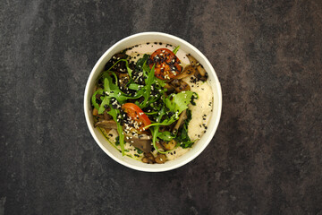 Vegan food. Breakfast oatmeal porridge with green herbs of mushrooms, tomatoes and sesame seeds on a dark background in an eco paper box. Healthy balanced food. Top view, overhead, banner