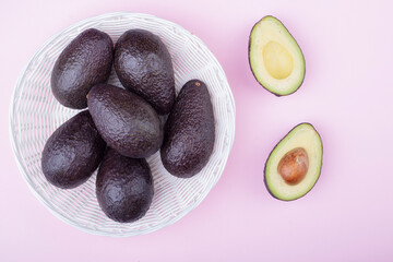 Ripe avocados in a fruit basket on a pink background. cut avocado