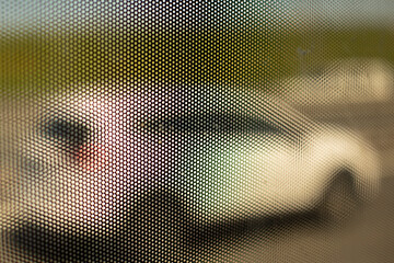 Mesh structure on glass of bus. Surface details of small holes. Blurry background shot through...