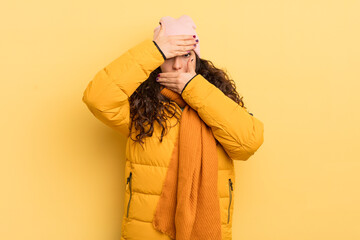 hispanic pretty woman covering face with both hands saying no to the camera! refusing pictures or...