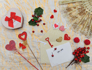 Greeting for a loved ones with a  gift box , a card with free space for writing on a gold textured background with a cream lace fan, red berries , hearts. Flat lay top view