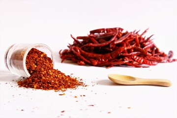 Chili pepper powder cup lying on the floor with wooden spoon and pile of chili peppers beside. stock photo isolate on white front view copy space  