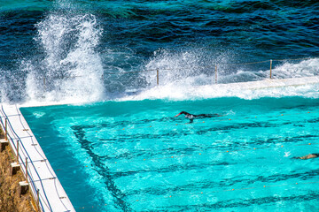 Swimmer in a pool along the ocean with waves crushing.