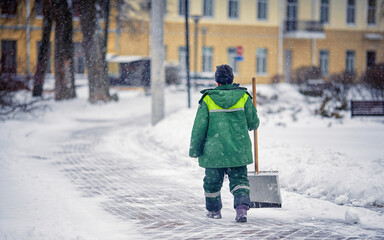 Worker with snow shovel sweep and remove snow, snow removal city service. Janitor in uniform with...