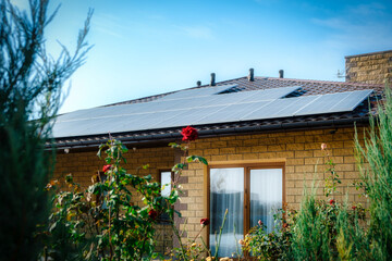 Backyard house with solar panels on the roof and green bush, flowers in stylish home