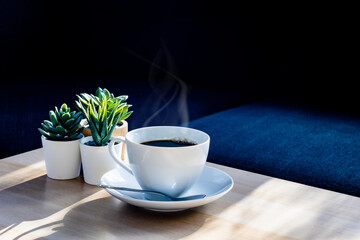 Top view a cup of hot coffee with steaming above the cup setting on wooden table under morning light near the window, coffee background with copy space relaxing moment concept.