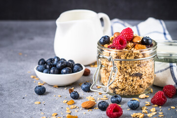Granola with fresh berries in the glass jar. Healthy dessert or snack at stone table.