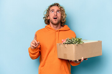 Young caucasian man making a move while picking up a box full of things isolated on blue background...
