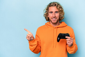 Young caucasian man playing with a video game controller isolated on blue background smiling and...
