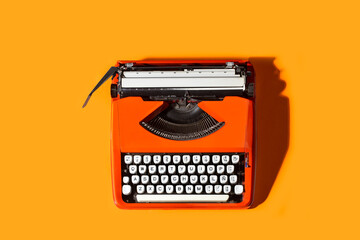 Máquina de escribir retro naranja de los años 60/70 sobre un fondo anaranjado. Vista superior. Copy space - obrazy, fototapety, plakaty