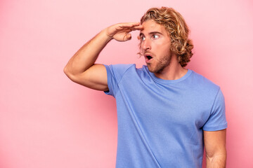 Young caucasian man isolated on pink background looking far away keeping hand on forehead.