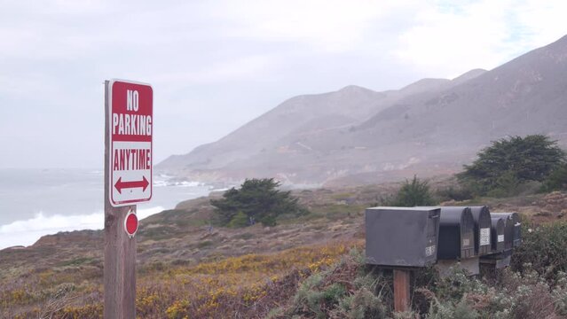 No parking any time road sign on pacific coast highway 1. Postbox or mailbox, Cabrillo road. Ocean sea waves on Garrapata beach, California, Big Sur nature trail, USA. Mountains, foggy misty weather.