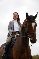 Fototapeta premium Beautiful young woman riding a horse on the field. Sideways to the camera. Freedom, joy, movement
