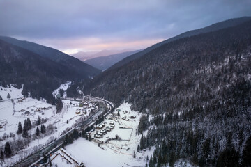Mountains covered with forest and road in the valley. Gloomy, dark winter weather.