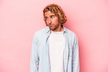 Young caucasian man isolated on pink background shrugs shoulders and open eyes confused.