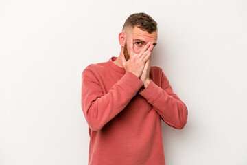 Young caucasian man isolated on white background blink through fingers frightened and nervous.