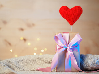 Gift box with pink ribbon on wooden background with copyspace. Red knitted heart. Valentine's Day gift concept
