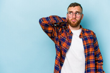 Young caucasian man isolated on blue background touching back of head, thinking and making a choice.