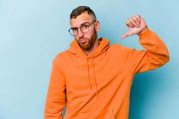 Young caucasian man isolated on blue background showing a dislike gesture, thumbs down....