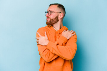 Young caucasian man isolated on blue background hugs, smiling carefree and happy.