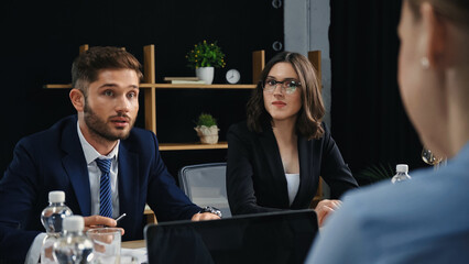 young business people looking at blurred colleague near laptop with blank screen