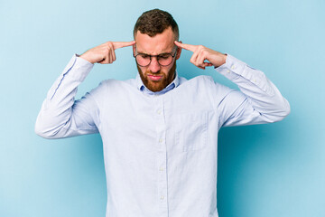 Young caucasian man isolated on blue background focused on a task, keeping forefingers pointing head.