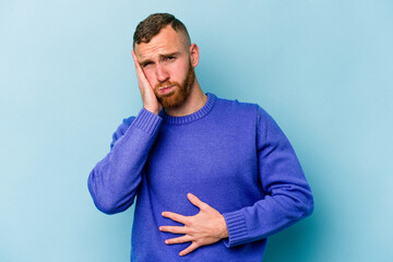 Young caucasian man isolated on blue background blows cheeks, has tired expression. Facial...