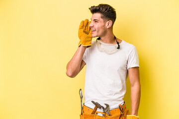 Young electrician caucasian man isolated on yellow background is saying a secret hot braking news and looking aside - obrazy, fototapety, plakaty