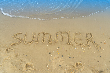 The word summer is written on the yellow sand of the beach. Blue wave and surf. Resort and vacation. Summer on the seaside. Relaxation rest concept.