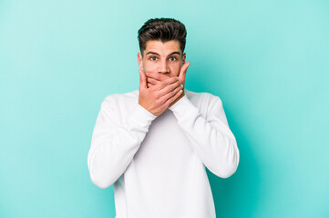 Young caucasian man isolated on blue background covering mouth with hands looking worried.