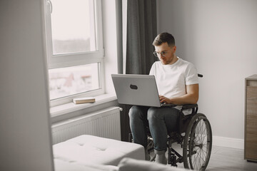 Young man in wheelchair using laptop working at home