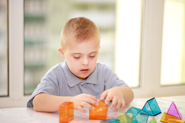 A boy with Down's syndrome plays with geometric figures, a plastic constructor, type 21 trisonomy,...