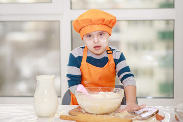A boy prepares dough from flour and milk, a child dressed as a cook cooks in the kitchen.
