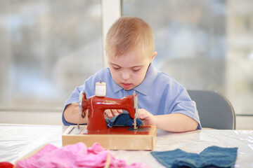 A boy with Down's syndrome sews clothes for dolls, a disabled child with type 21 trisonomy, an extra chromosome, a special child.
