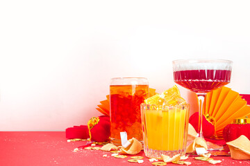 Chinese New Year Cocktail drinks, set of three different glass with various red gold color alcohol party beverage, with traditional Chinese New Year decor, greeting envelopes, Chinese lanterns, coins