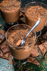 Homemade chocolate panna cotta dessert. Dark and milk chocolate panna cotta in portioned glasses, traditional Italian dairy dessert over dark background, with chocolate drops, slices and shavings